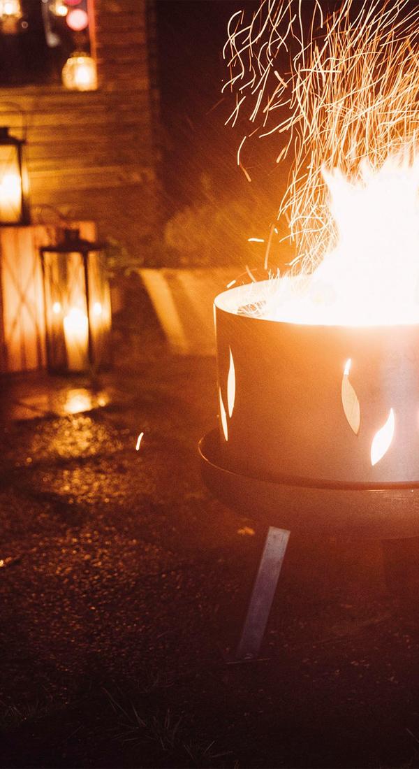 Stimmungsvolle Abendaufnahme mit einem brennenden Feuerkorb und mehreren Laternen im Hintergrund.