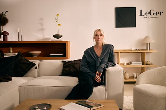 LeGer Home by Lena Gercke – Frau sitzt auf Sofa in modernem Wohnzimmer mit Regalen und Couchtisch