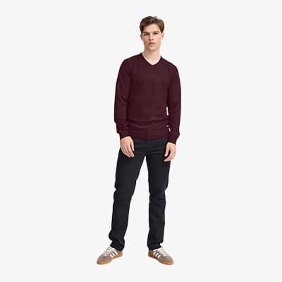 Mann in dunkelrotem Pullover, schwarzer Hose und Turnschuhen steht frontal in die Kamera