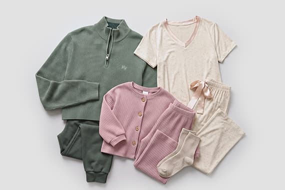 Kinder-Outfit mit grünem Sweatshirt und Hose, rosa Strickjacke und Hose, weißes T-Shirt, Shorts und Socken