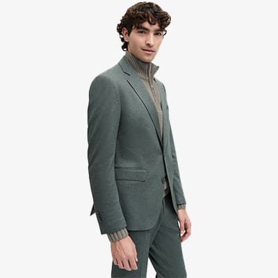 Mann in grauem Anzug und grauem Rollkragenpullover steht seitlich und schaut nach vorne