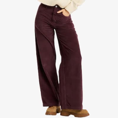 Frau trägt weinrote Schlaghose und beige Pullover, steht mit einer Hand in der Hosentasche