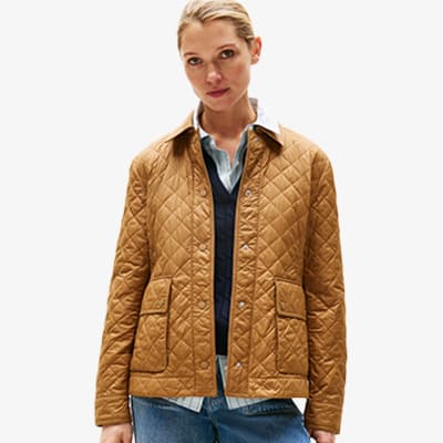 Person trägt eine gesteppte, braune Jacke über einem Hemd und Pullover, dazu blaue Jeans