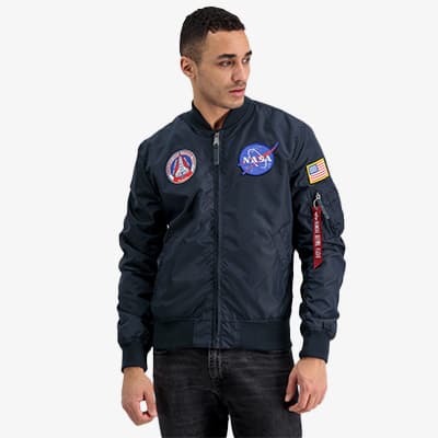 Person in dunkelblauer NASA-Jacke mit Abzeichen und US-Flagge, steht mit Händen seitlich und Gesicht unkenntlich gemacht