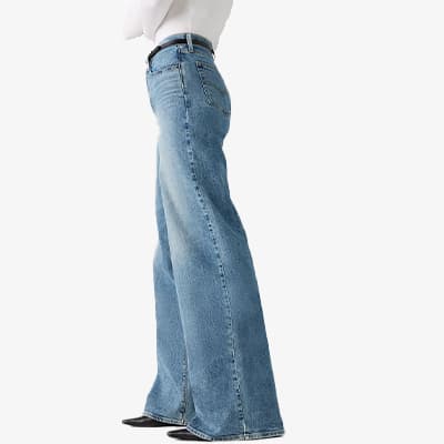 Frau trägt hellblaue, weit geschnittene Jeans mit hohem Bund und weißem Oberteil, seitliche Ansicht