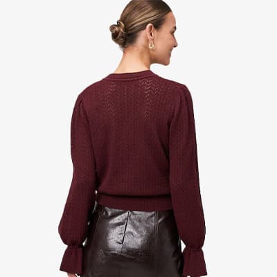 Frau mit Dutt trägt bordeauxfarbenen Strickpullover und glänzenden schwarzen Rock, Rückenansicht