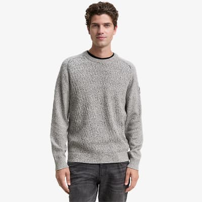 Mann in grauem Strickpullover und dunkler Jeans, steht gerade und zeigt die Vorderseite des Pullovers