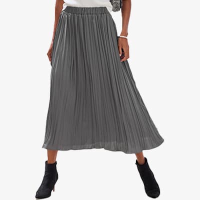 Frau trägt einen langen, grauen Plisseerock und schwarze Stiefeletten. Hände in Hüfte gestützt. Rock fällt fließend.