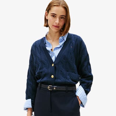 Frau trägt dunkelblauen Cardigan über hellblauer gestreifter Bluse und dunkler Hose mit Gürtel. Gesicht ist unscharf.