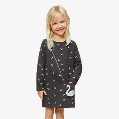 Kind mit blondem Haar trägt ein schwarzes Kleid mit weißen Mustern und einer Schwanentasche auf der linken Seite.