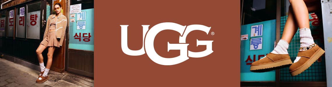 UGG - Frau in beiger Jacke und Rock lehnt an Wand, trägt braune UGG-Schuhe und weiße Socken
