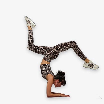 Frau in Leopardensportkleidung macht Handstand, Beine in der Luft gespreizt, Gesicht unscharf, trägt weiße Turnschuhe