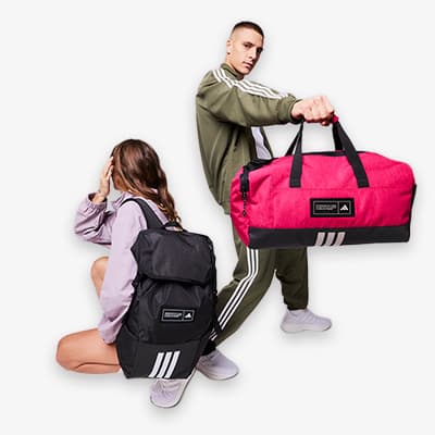 Zwei Personen in sportlicher Kleidung – eine sitzt und trägt einen schwarzen Rucksack, die andere steht und hält eine rote Sporttasche