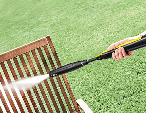 Person reinigt Holzstuhl im Garten mit Hochdruckreiniger