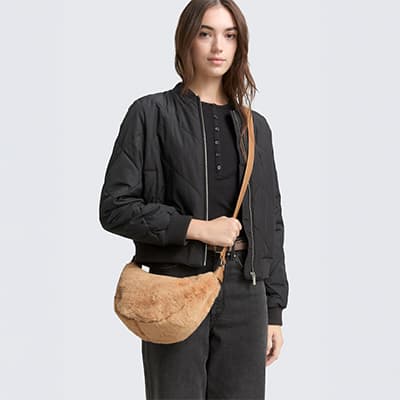 Frau in schwarzer Jacke und dunkler Hose trägt eine braune Umhängetasche