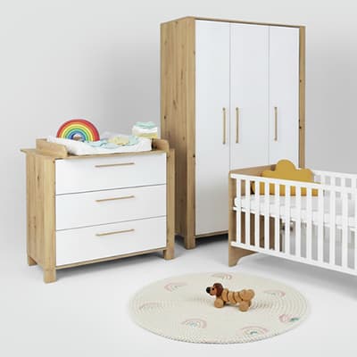 Holz-Kleiderschrank, Wickelkommode mit Regenbogen, Babybett und runder Teppich mit Regenbogenmuster in einem Kinderzimmer