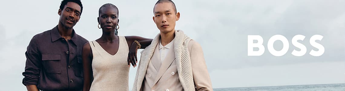 BOSS – Drei Personen stehen am Strand, tragen modische, neutrale Kleidung und schauen in die Kamera.