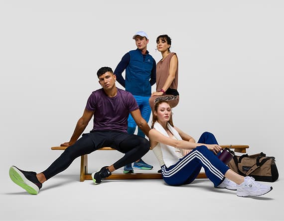 Vier Personen in Sportkleidung, sitzen und stehen auf einer Bank, eine Sporttasche daneben.