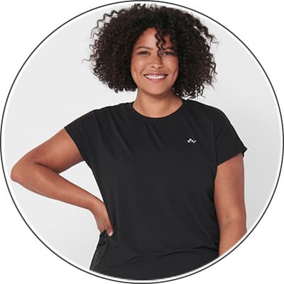 Frau mit lockigem Haar trägt ein schwarzes T-Shirt und steht vor einem weißen Hintergrund.