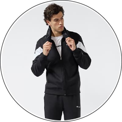 Mann in schwarzer Trainingsjacke mit weißen Streifen, hält den Kragen und trägt schwarze Hose.
