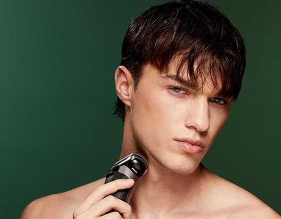 Mann rasiert sich mit einem elektrischen Rasierer vor grünem Hintergrund.