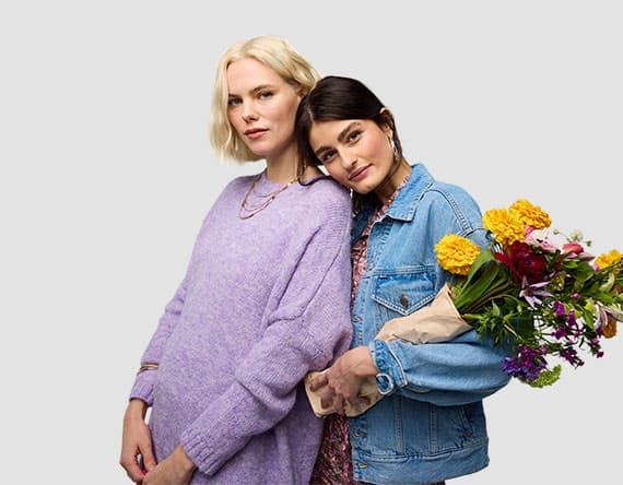 Zwei Personen stehen nebeneinander, eine hält einen Blumenstrauß, die andere trägt einen lila Pullover.