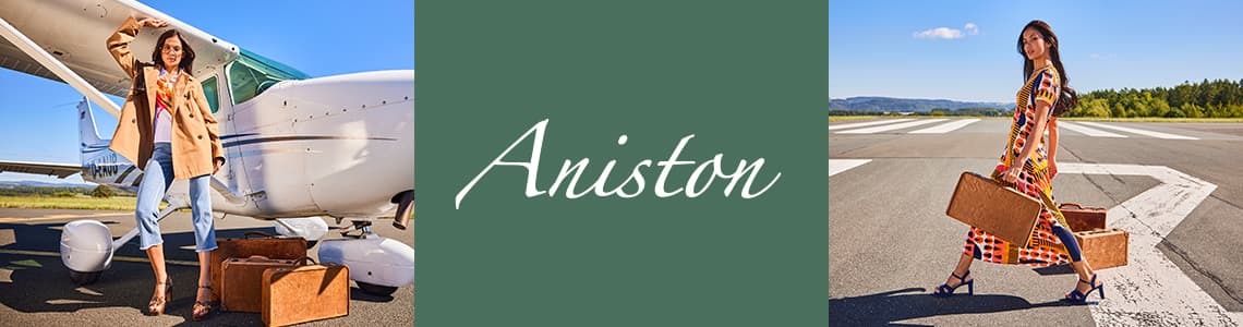 Aniston – Frau in beigem Mantel und Jeans steht vor Flugzeug. Frau in buntem Kleid trägt zwei Koffer auf Flugfeld.