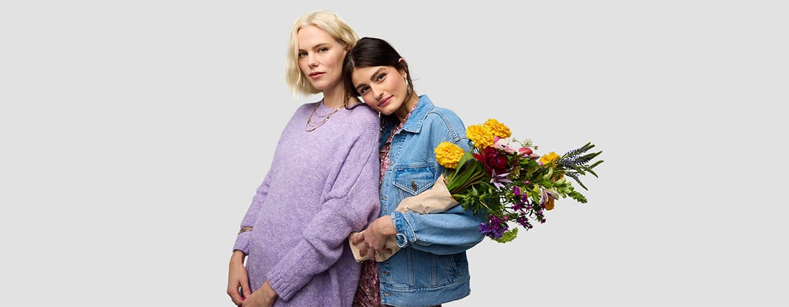 Zwei Personen umarmen sich, eine hält einen bunten Blumenstrauß.