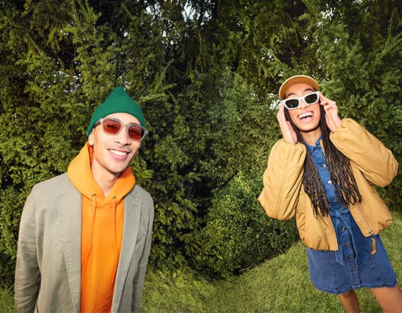 Zwei Personen in bunter Freizeitkleidung stehen im Grünen vor dichten Büschen