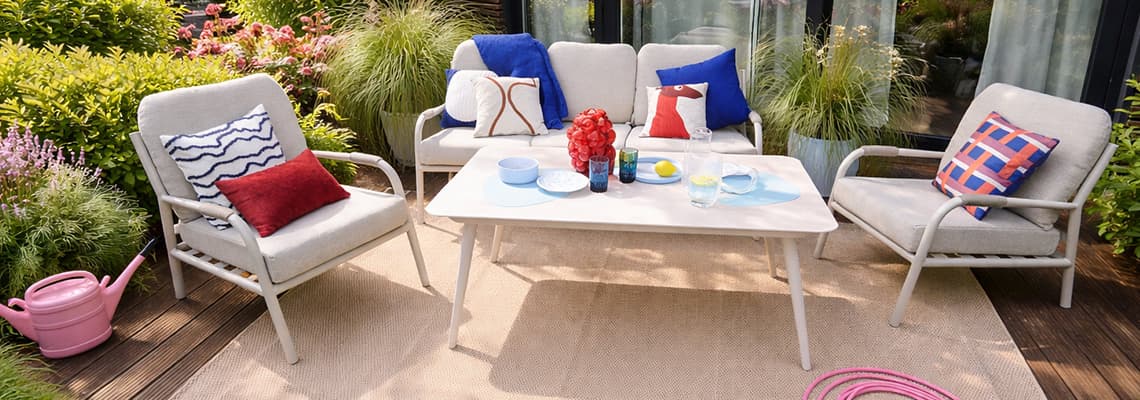 Gemütliche Gartensitzgruppe mit Sofa, zwei Sesseln und bunten Kissen um einen gedeckten Tisch auf Terrasse