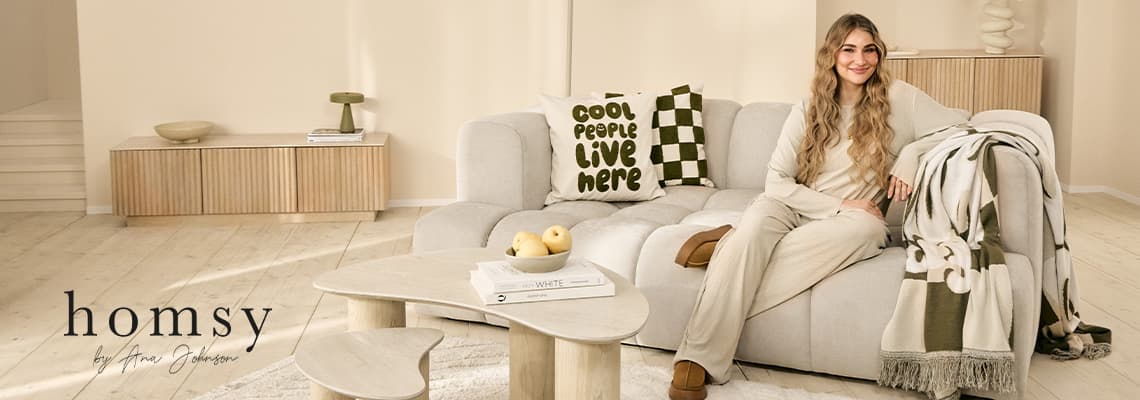 Kissen mit Aufdruck „cool people live here“ auf Sofa, daneben Frau in heller Kleidung in modernem Wohnzimmer