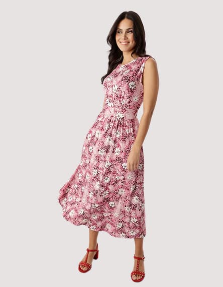 Frau im knöchellangen rosa Blumenprint-Kleid mit breiten Trägern und rosanen Sandalen steht leicht seitlich zur Kamera