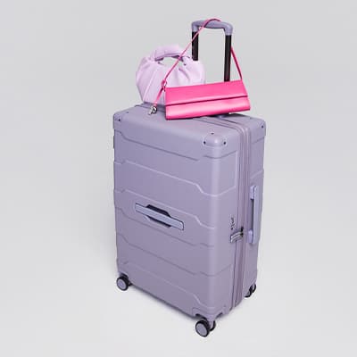 Großer lilafarbener Rollkoffer mit ausgezogenem Griff, darauf eine rosa Handtasche und ein pinkes Schultertäschchen