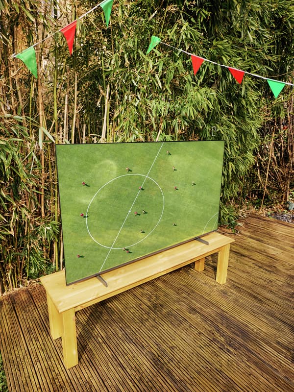 Garten mit Lounge-Sitzgruppe und bunten Kissen, gedecktem Tisch, Grill im Hintergrund und Fußball im Gras