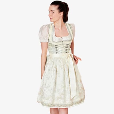 Frau im knieumspielenden Dirndl mit Schürze und Schnürung, steht seitlich und blickt aus dem Bild