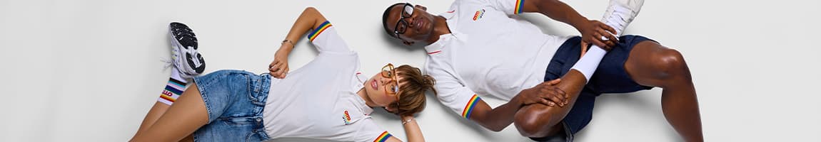 Zwei Personen liegen entspannt nebeneinander in weißen Poloshirts mit Regenbogenstreifen und passenden Socken
