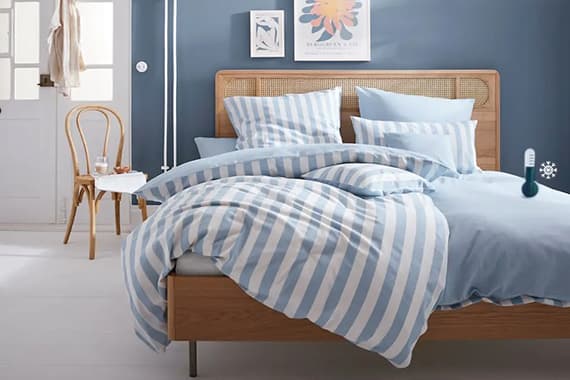 Bett mit blau-weiß gestreifter Bettwäsche, mehreren Kissen und Holzrahmen in modernem Schlafzimmer mit Stuhl und Wandbild