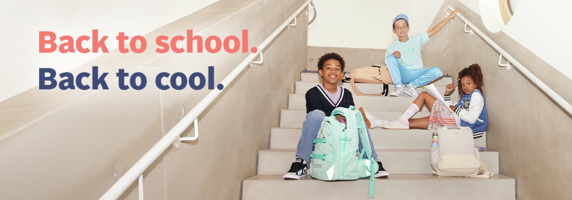 Back to school. Back to cool. – drei Kinder mit bunten Rucksäcken sitzen auf einer Treppe und schauen in die Kamera