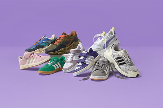 Mehrere bunte adidas Sneaker in verschiedenen Designs stehen nebeneinander vor lila Hintergrund