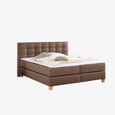 Doppelbett mit hohem, gepolstertem Kopfteil, Bettdecke und zwei Kissen, freistehend vor hellem Hintergrund