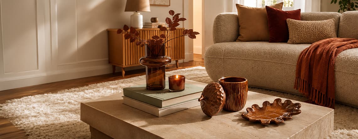 Wohnzimmer mit beiger Couch, herbstlichen Kissen und Deko in Brauntönen auf einem Couchtisch mit Büchern und Vasen