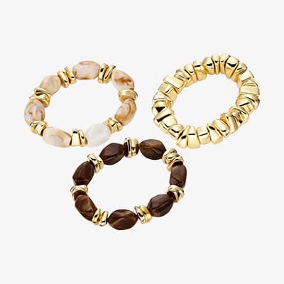 Drei elastische Armbänder mit goldfarbenen Gliedern und beige bis dunkelbraunen Schmucksteinen auf weißem Hintergrund